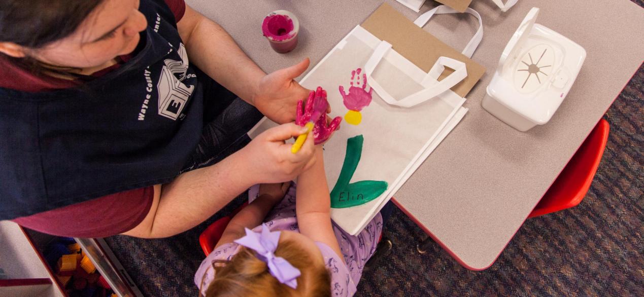 Image of preschooler finger painting with student
