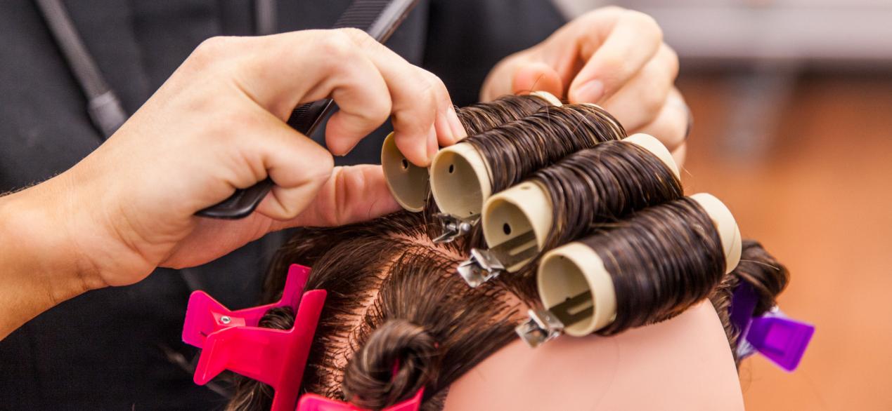 Image of student puts rollers in mannequin's hair