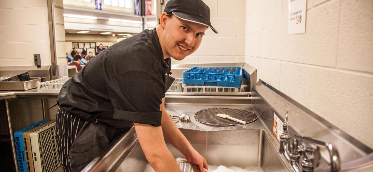 Image of student happily washing dishes
