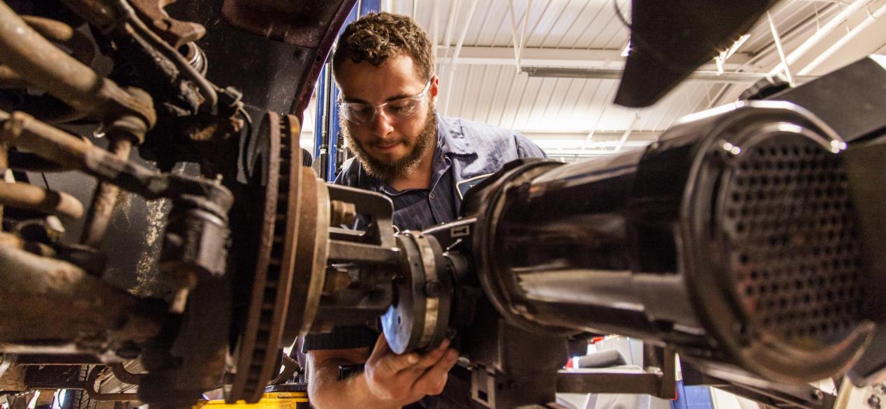 Image of student working on mechanics of a car