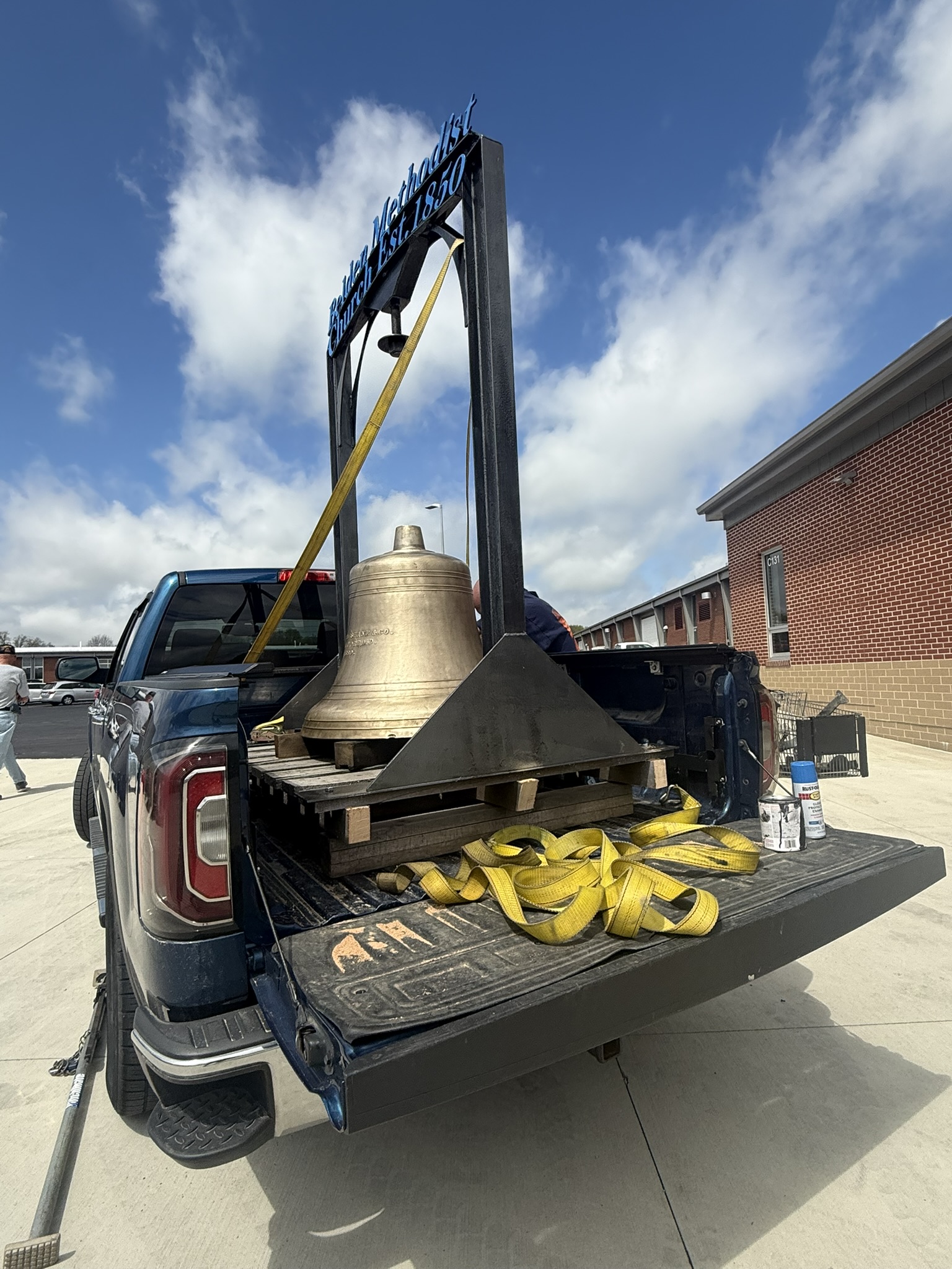 A pickup truck with a church bell on a stand inside ready to be delivered