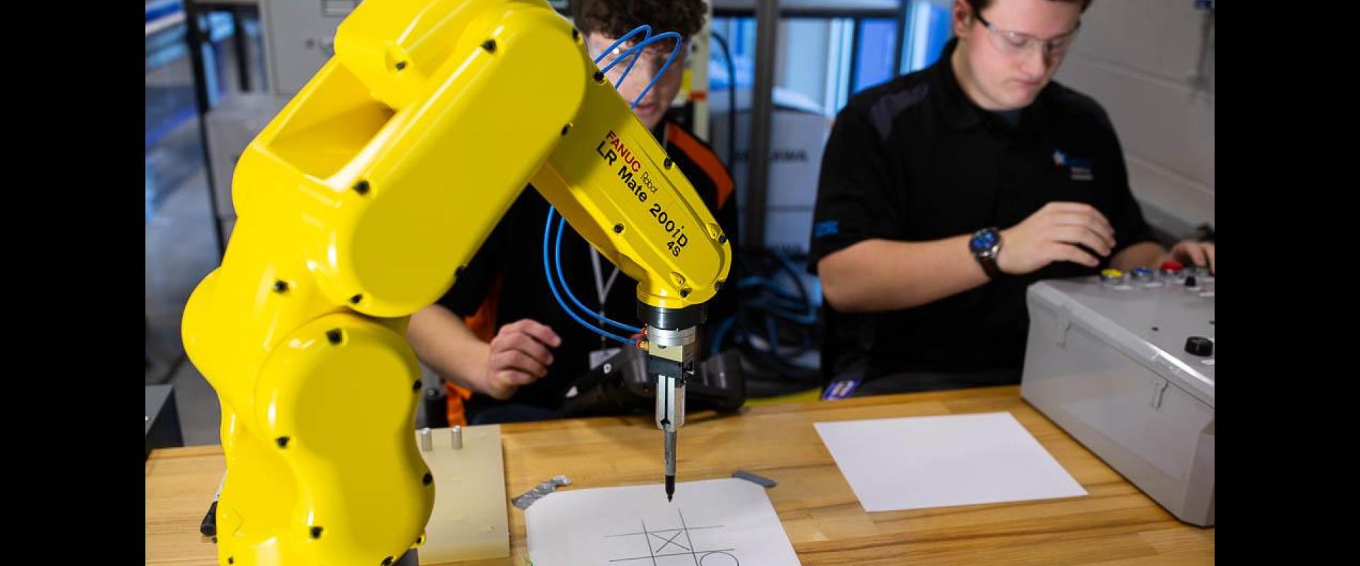 Two engineers working with a robot who is playing tic-tac-toe