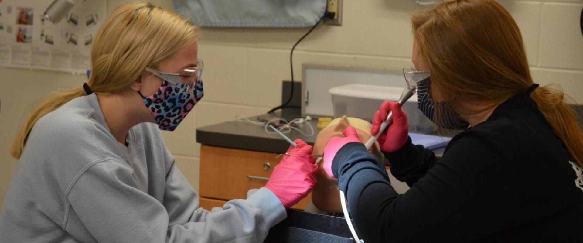 Two students working on the mouth of a practice dummy
