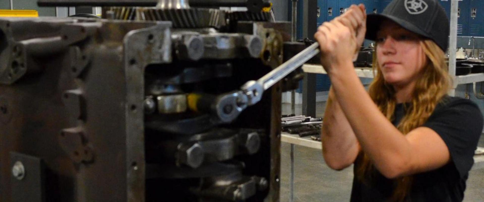 A woman mechanic tightening the bolt of an engine