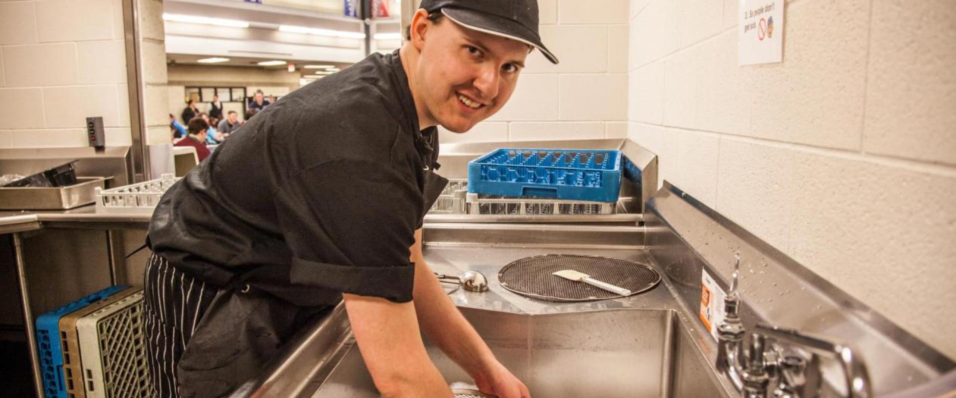 A males washing dishes in a restaurant style sink