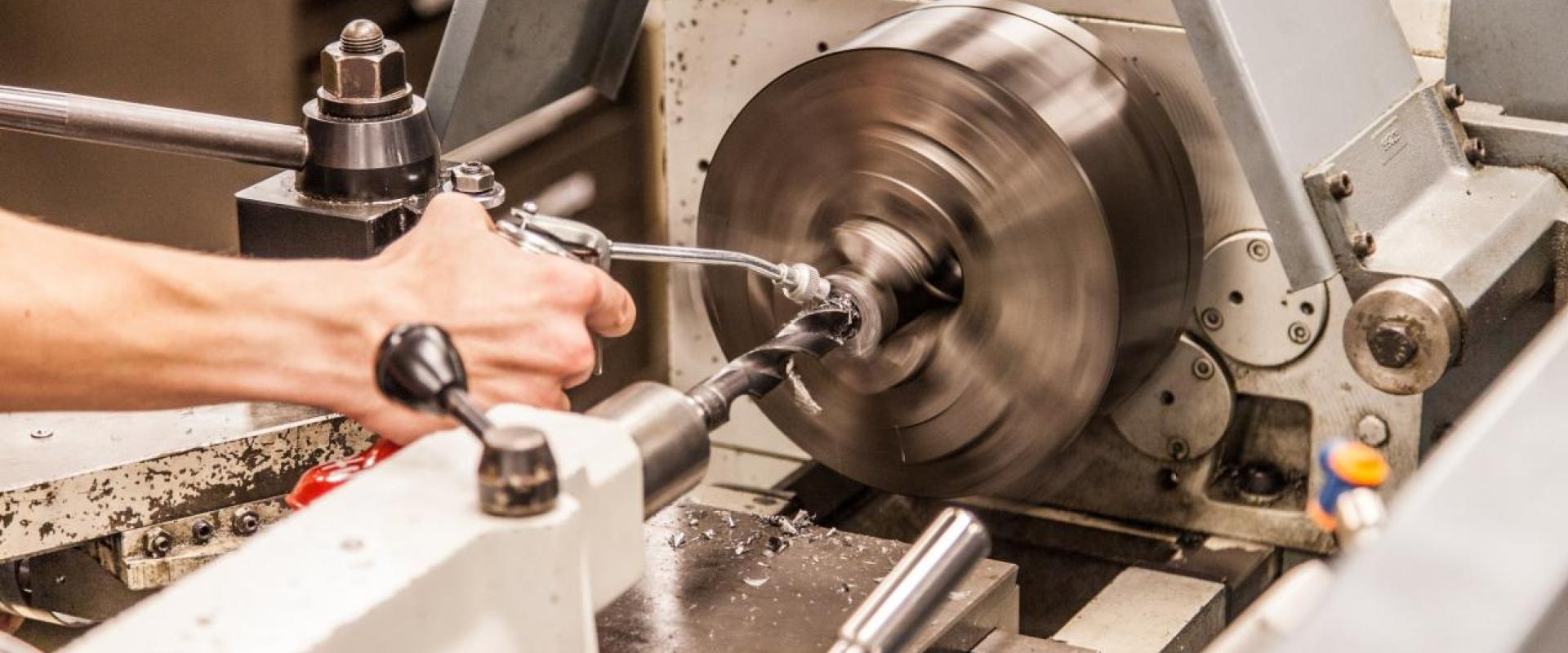 A hand oiling a part on a machine lathe