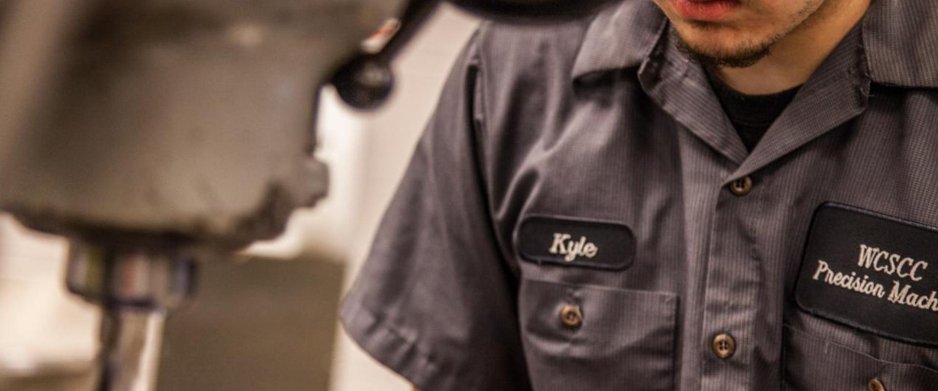 A person with the name tag "Kyle" working at a vertical drill lathe