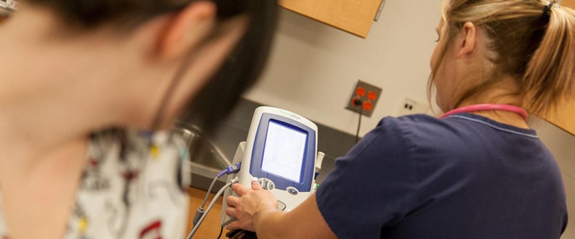 A nurse changing the settings on a blood pressure machine