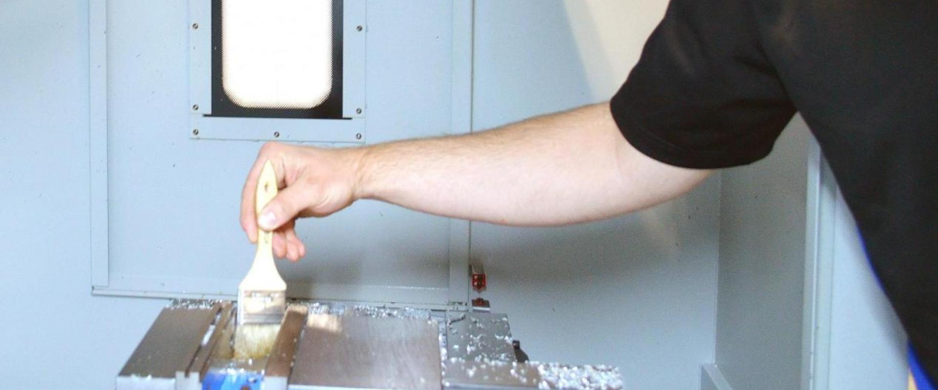 An individual brushing metal shavings from the inside of a CNC machine