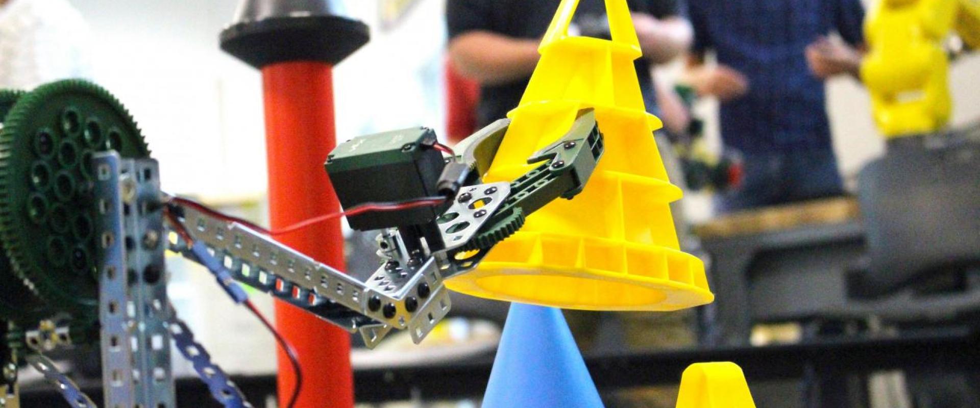 A student built VEX robot moving a cone with students in the background