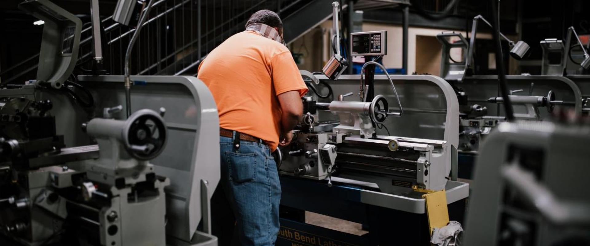 A man with his back turned working at a machine lathe