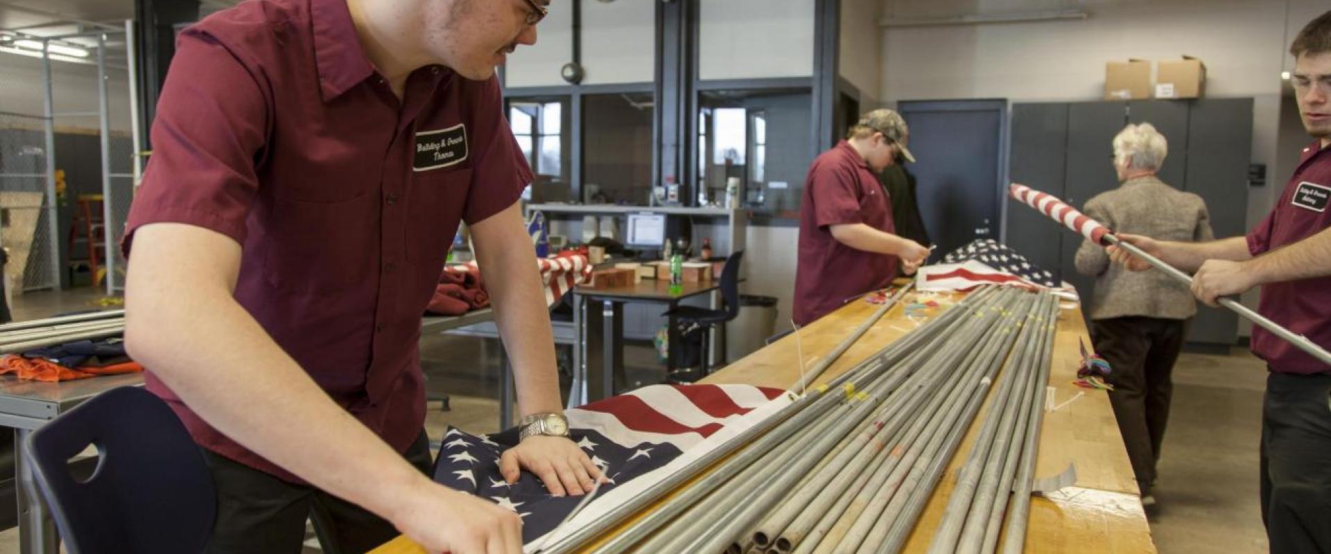 Three students assembling USA flags to flag poles.
