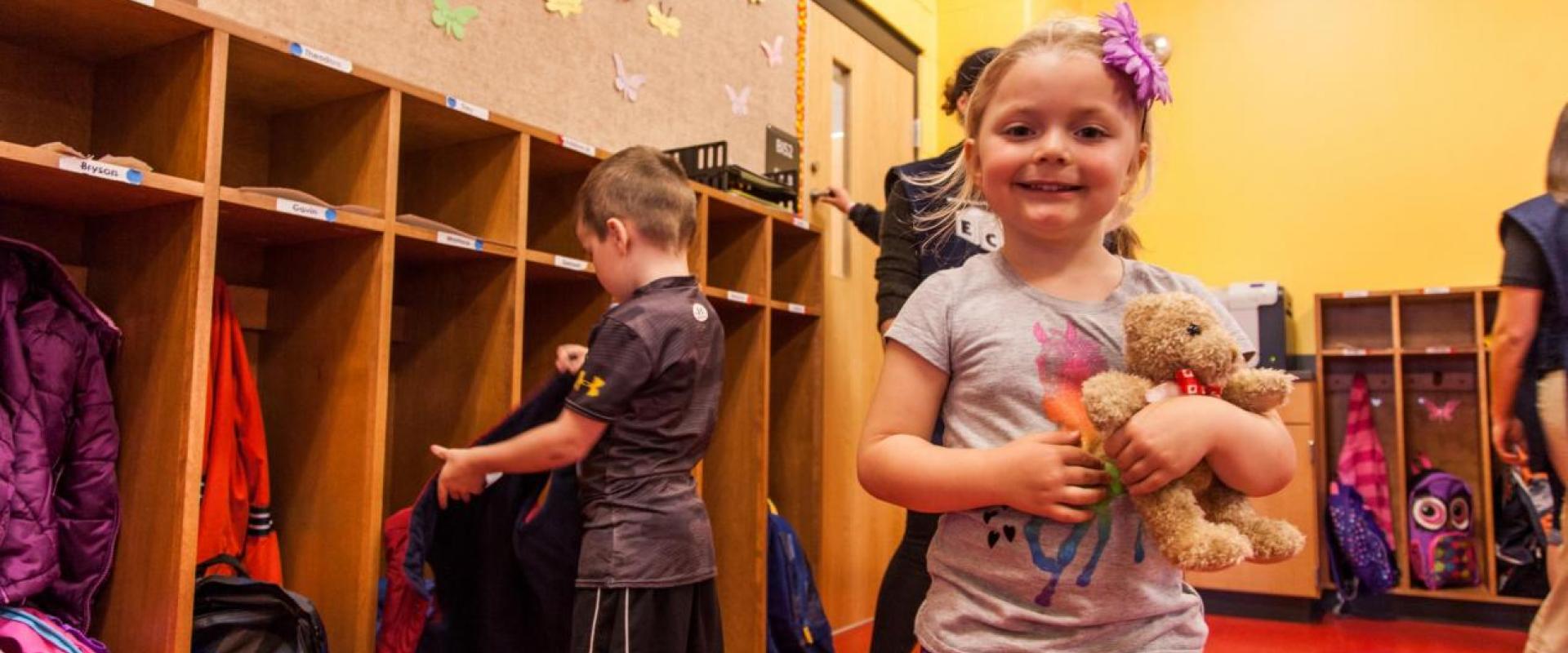 A young girl holding a teddy bear in a daycare setting