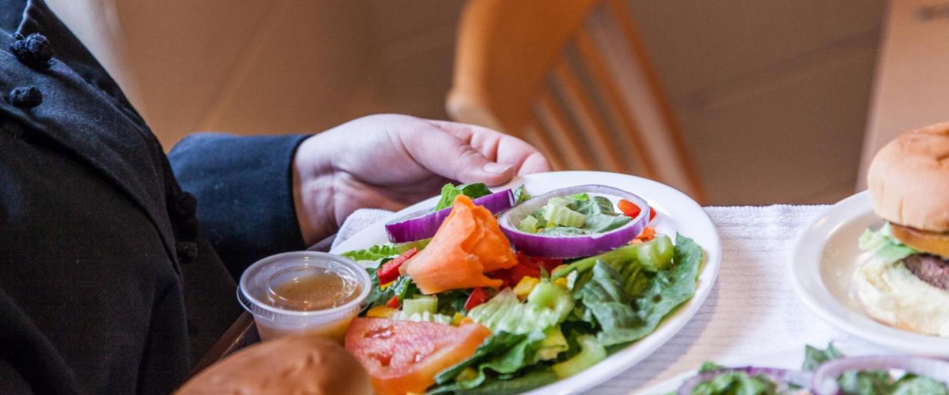 A student serving a salad and a burger in the student ran restaurant 