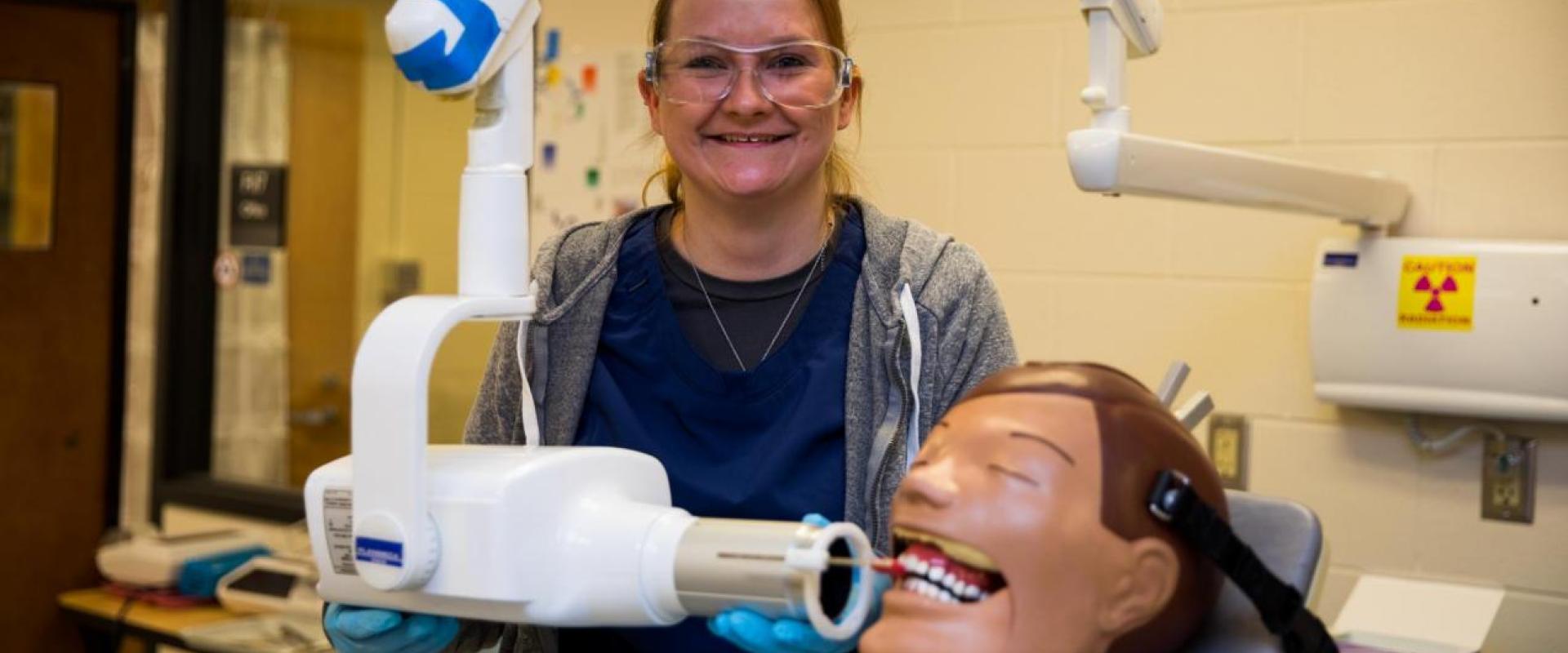 A student holding a dental exray machine up to the mouth of a test dummy