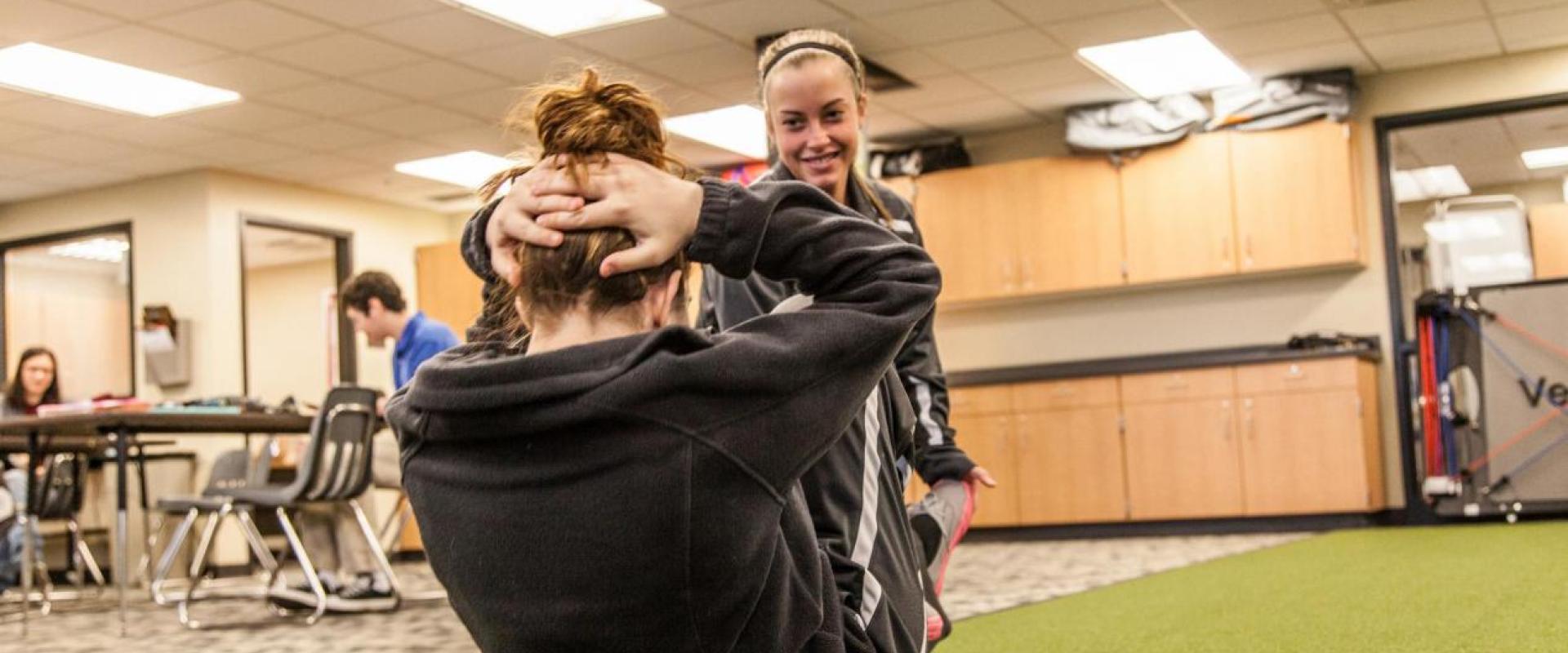 A girl assist another individual with a crunch. 