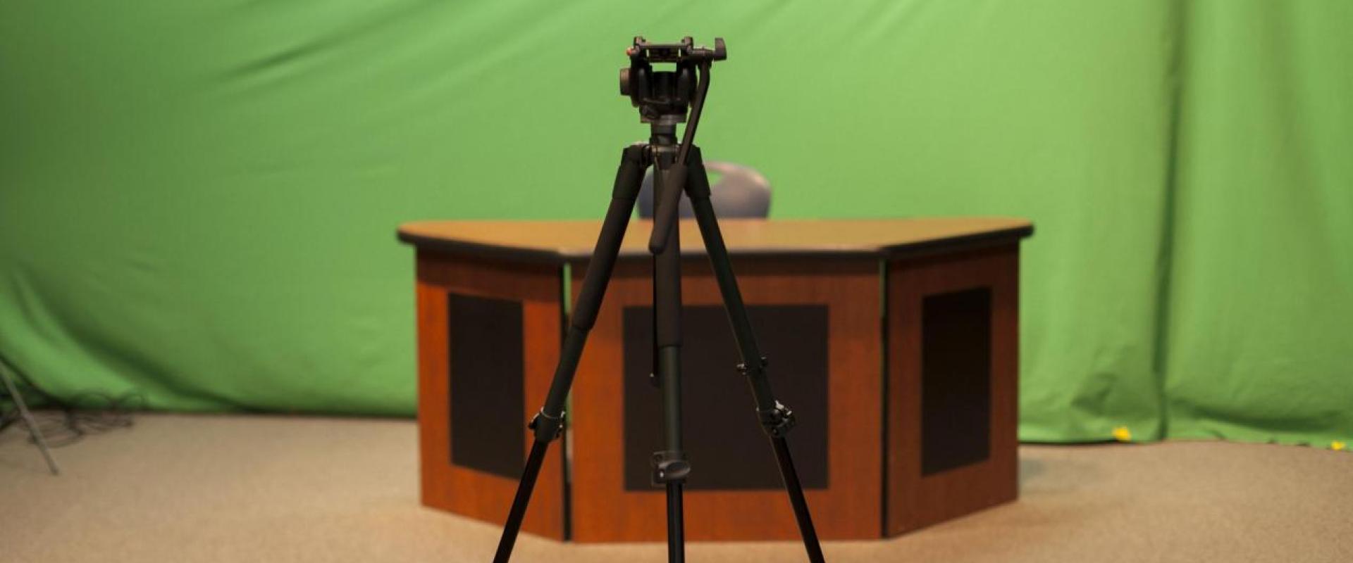 a camera stand in front of a news desk in front of a green screen 