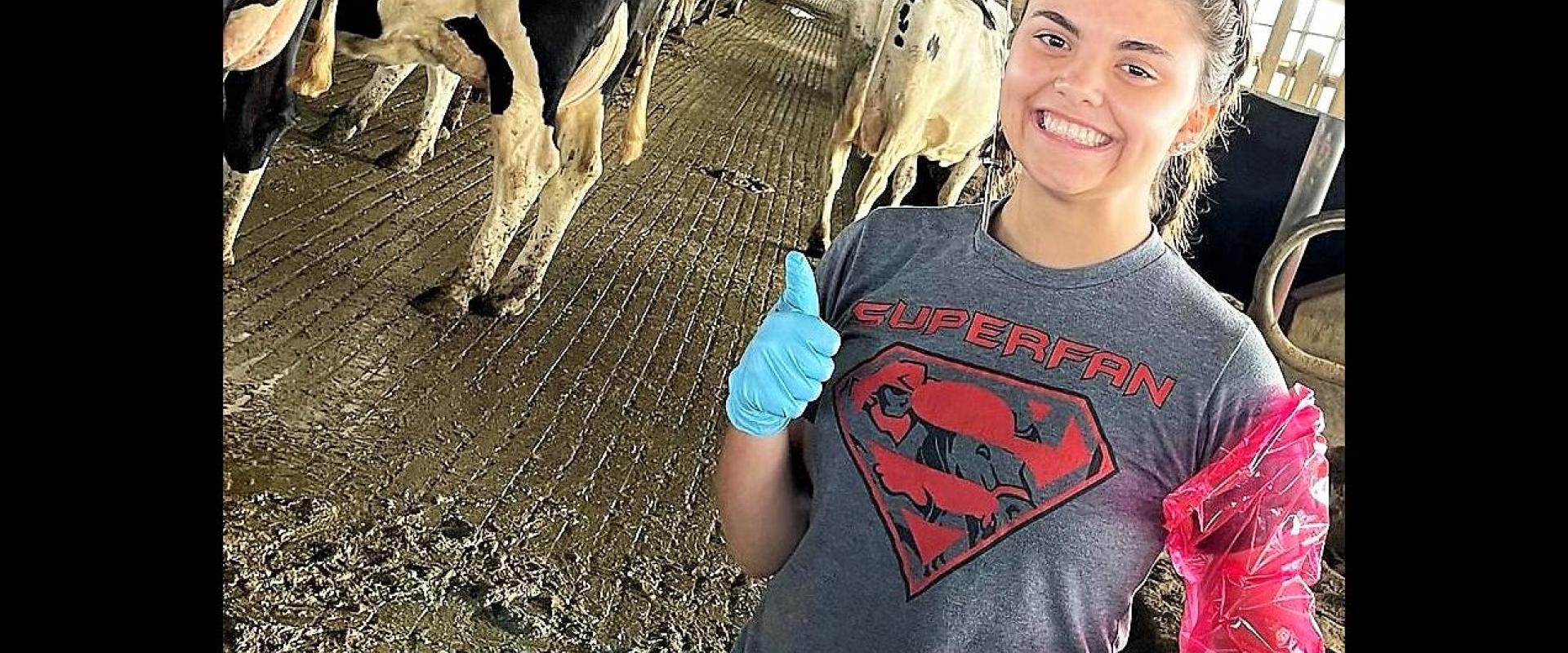 A girl with a thumbs up in front of dairy cows