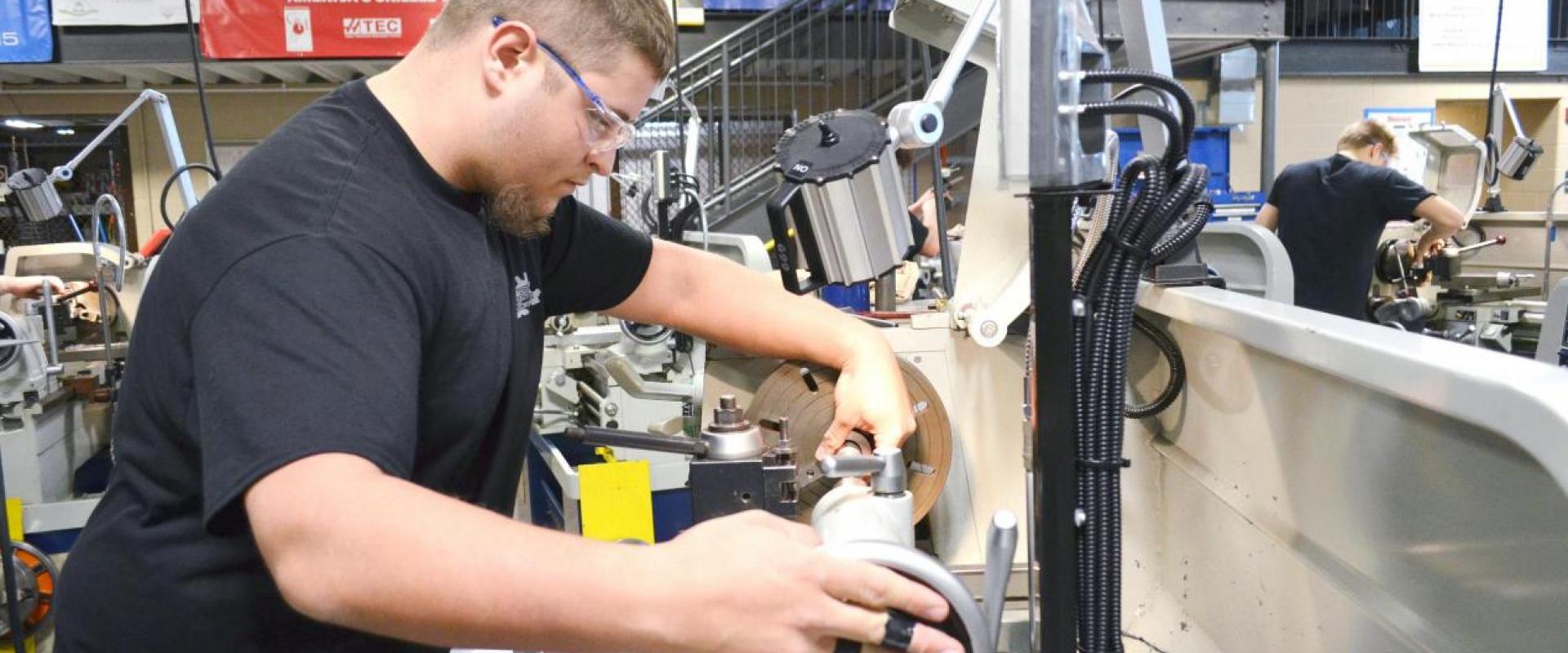 A male adjusting a piece on a machine lathe