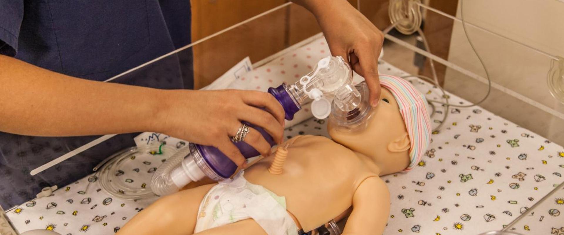 An individual adjusting a breathing mask on test dummy infant 