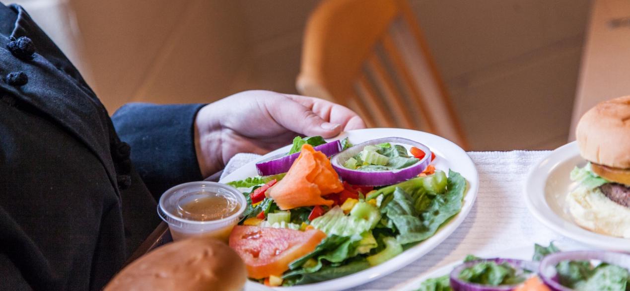 Image of student serving lunch of a salad and a burger in the student-run restaurant 