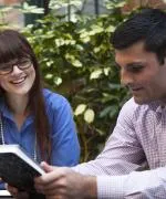 Man holding book while woman smiles and reads the book.