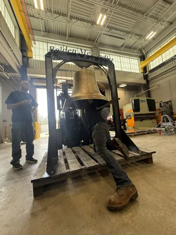 a student helps secure a church bell to a stand with guidance from adults
