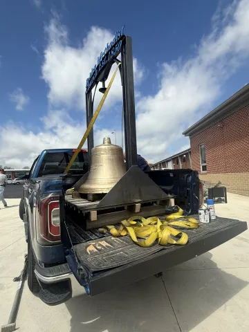 A pickup truck with a church bell on a stand inside ready to be delivered